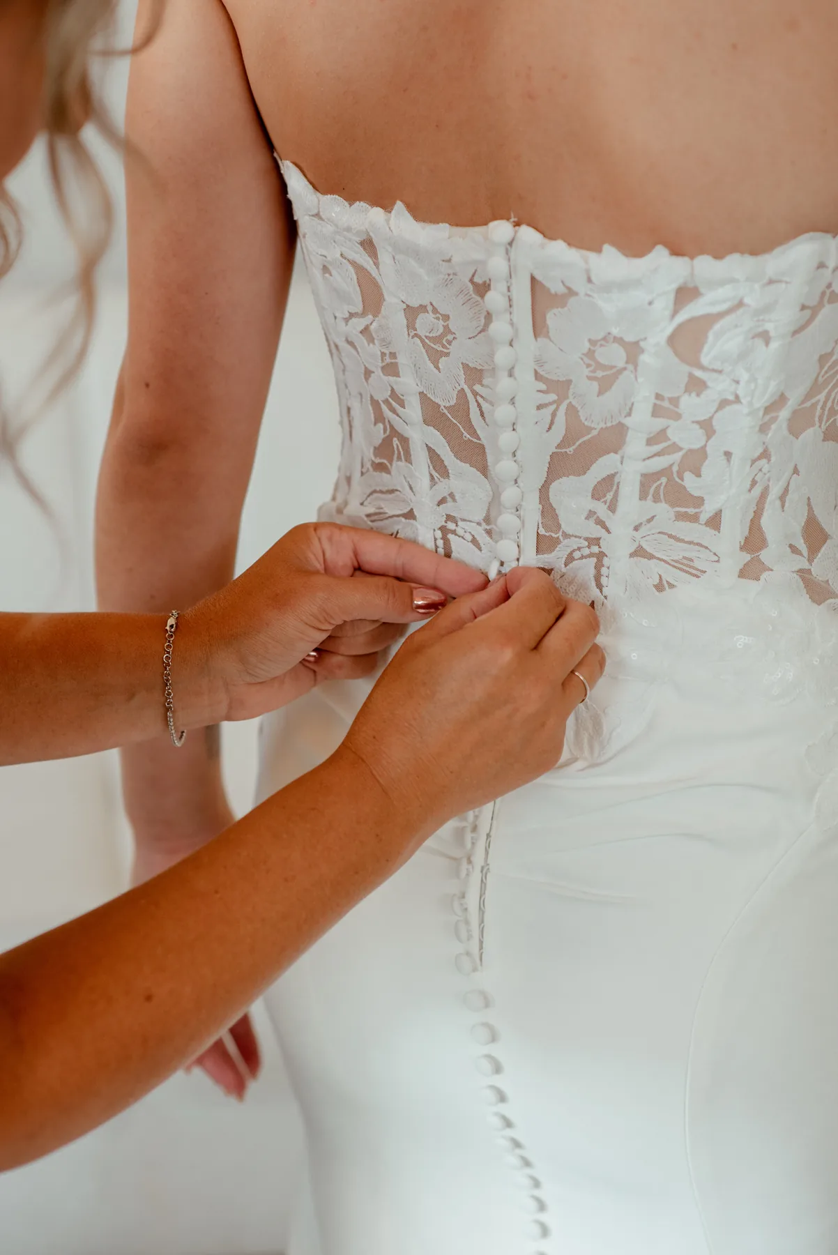 Hands fastening the buttoned back of a lace bridal gown